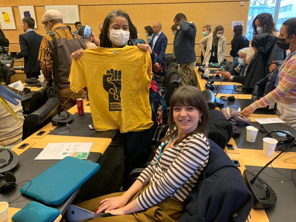 Luciana Viegas, do Vidas Negras com Deficiência Importam (à esquerda, segurando uma camiseta amarela do VNDI) e Lauren Avery, do Minority Rights Group (no centro, à direita, sentada) em Genebra, Suíça, apresentando o relatório alternativo ao Comitê da ONU para a Eliminação de Discriminação racial.